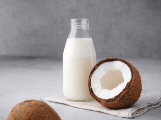 Coconut vegan milk is non dairy products in a bottle with a place to copy on a gray concrete background. Glass bottle of milk or yogurt with coconut chips aside. Concept of healthy eating. Close up.