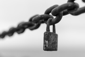 Closeup of a rusted metal lock hanging from a metal chain on a blurry background