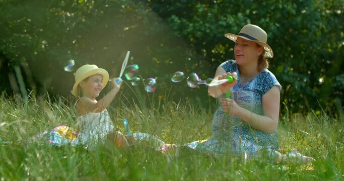 Mother and daughter blow soap bubbles in the park.
