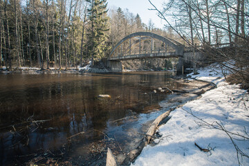Fototapeta na wymiar Old bridge across the river Spring landscape in April of a forest river. Snow lies on the shore. Finland.