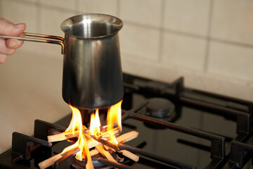 The rise in price of the gas tariff. A woman's hand holds a cup of coffee over the kitchen stove. Instead of gas, firewood is burning on the gas burner. Selective focus.