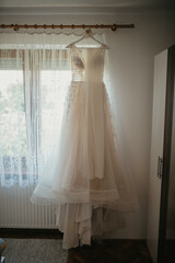 Wedding dress hanging in the room. Scenery for the morning of the bride with a white wedding dress and a bouquet.