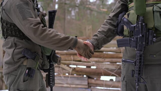 Two unrecognizable male soldiers shaking hands standing outdoors. Courageous Caucasian young men defending country independence in Ukraine in war zone. Handshake of brave warriors - Powered by Adobe