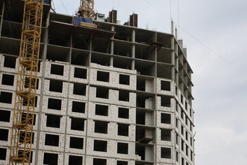Fototapeta premium Construction yellow crane builds a tall multi-apartment residential building from white bricks and concrete slabs. Construction of a residential complex in the city center
