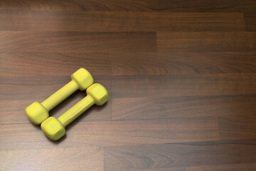 Two yellow dumbbells lie diagonally on the parquet floor, physical exercises at home and in the fitness club