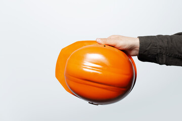Close-up of male hand holding a hardhat of orange color, on white background.