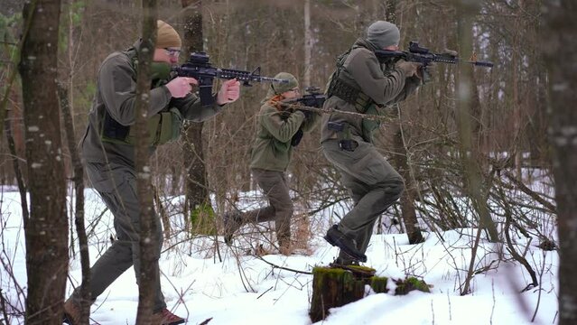 Wide shot courageous young armed men and women walking in winter forest in war zone in Ukraine. Side view tracking shot of brave Ukrainian soldiers warriors defending independence on military invasion