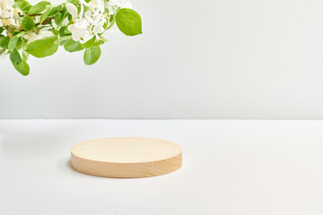 Empty round wooden podium for product presentation and spring flowers on a light background. Mockup...