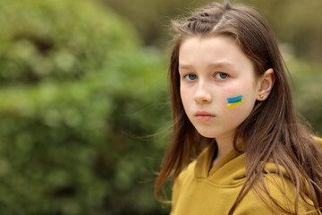 the face of a frightened girl, painted on her cheek in the yellow-blue colors of the Ukrainian flag, a request for help. Children ask for peace. High quality photo