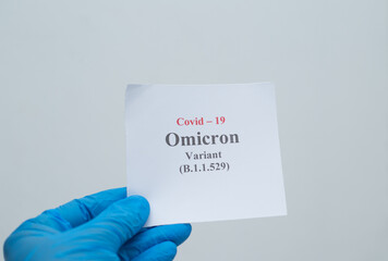 Closeup of a person wearing a latex glove and holding a COVID omicron variant note