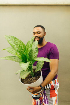 portrait of a smiling black male gardener holding his large green plant 