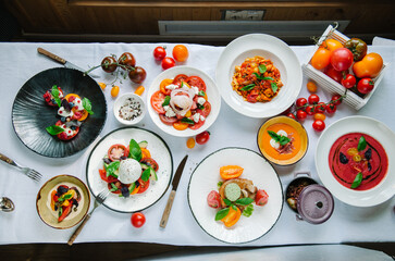Variety of dishes on the table. Tomato menu in the restaurant, tomato soup, mix of tomatoes with buffalo mozzarella and pesto, pork fillet with baked. Restaurant menu. Italian cuisine. Top view