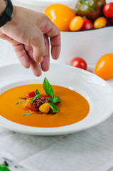 Delicious creamy tomato soup with herbs. Summer light yellow tomato soup. The chef's hand adds a basil leaf to the decor of the dish
