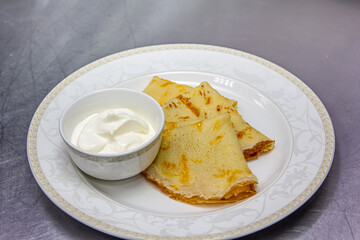 Traditional Russian pancakes folded in a triangle with sour cream are on a plate