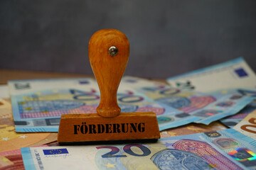 Holzstempel mit der Aufschrift Förderung und Euro Geldscheine