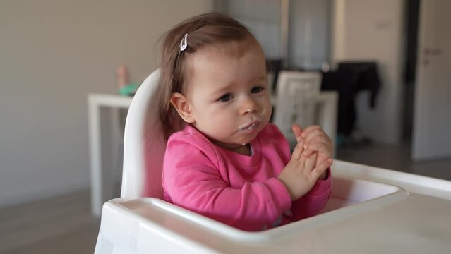 One baby small caucasian girl sitting in the feeding high chair while her unknown mother holding spoon with food real people side view child wear pink infant nutrition concept