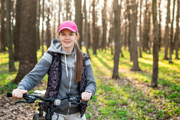 Happy young female holds steering wheel of her bike at the sunny spring forest