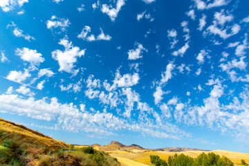 Andalusian landscape with yellow hills and blue sky with high white clouds