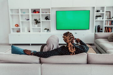 African Couple Sitting On Sofa Watching TV Together Chroma Green Screen Woman Wearing Islamic Hijab Clothes