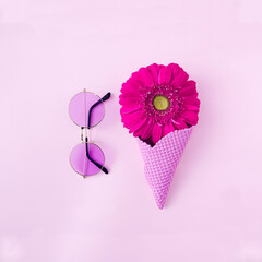 A pink ice cream cone with a magenta gerbera daisy and tinted pink sun glasses on pastel pink background. Creative concept for romantic spring summer season banner or advertisement.