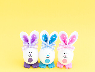 Three white creative eggs with painted eyes and multi-colored ears and paws on a yellow background in the center.