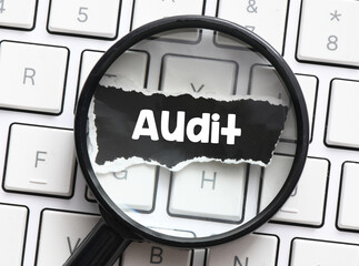 AUDIT word on a black sheet of paper under the magnifying glass.