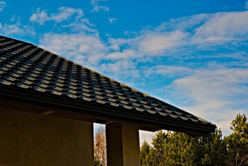 Dach z blachy , imitującej dachówkę ceramiczną , na świeżo zbudowanym domu na tle błękitnego nieba z białymi chmurkami ( obłokami)  . - obrazy, fototapety, plakaty