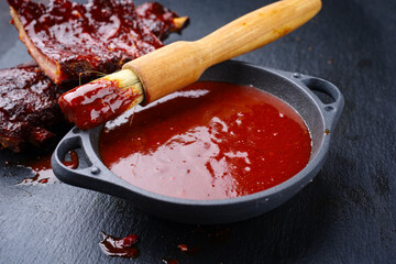 Hot and spicy barbecue sauce in a bowl as close-up with spare ribs in background - obrazy, fototapety, plakaty