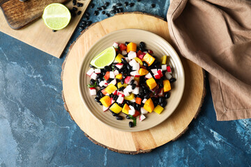 Plate of tasty Mexican salad with black beans and radish on blue background