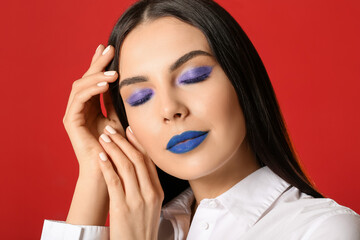 Beautiful young woman with creative makeup on red background