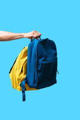 Male hand with backpacks in colors of Ukrainian flag on blue background