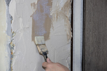 Preparing the wall for leveling with plaster. Priming a concrete wall with an old natural bristle...