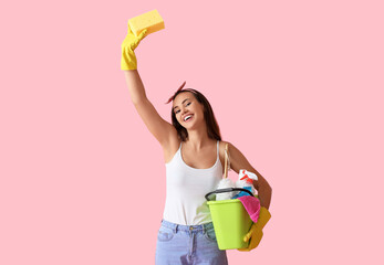 Young woman with cleaning supplies on pink background