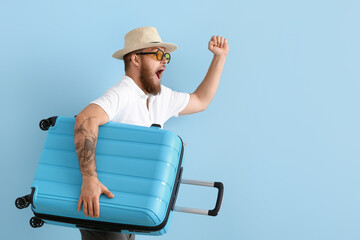 Happy young man in hat with suitcase on blue background