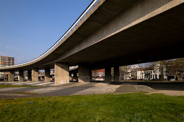 Obraz premium Overpass Arnhem intersection Onderlangs roundabout seen from below the concrete construction with apartment buildings in the background. Transportation and infrastructure engineering concept.
