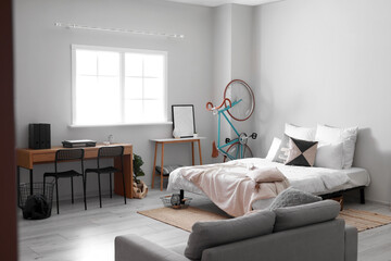Interior of light room with big bed, modern workplace and bicycle
