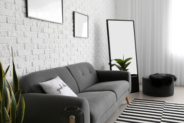 Comfortable sofa and mirror near white brick wall in living room