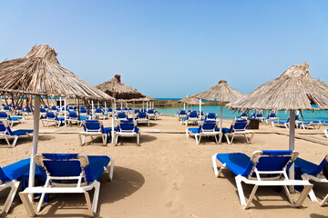 Empty beach with chairs, sunbeds, straw umbrellas, and blue sky. Mediterranean summer vacation...