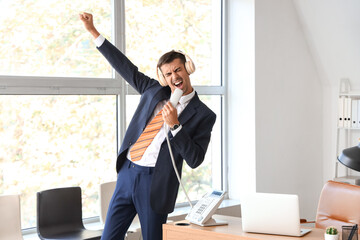 Young businessman with headphones singing in office