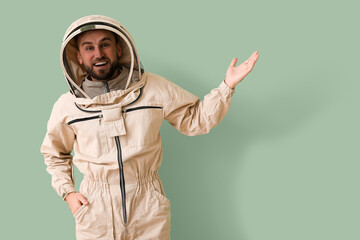 Male beekeeper in protective suit showing something on green background
