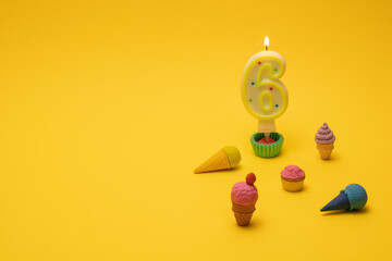Birthday candle number six with  toys of cookies and ice cream on a yellow background. Birthday...