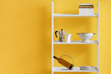 Modern shelving unit with dishware near yellow wall in kitchen