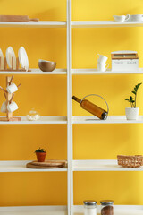 Modern shelving unit with dishware near yellow wall in kitchen
