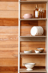 Modern shelving unit with dishware near wooden wall in kitchen, closeup