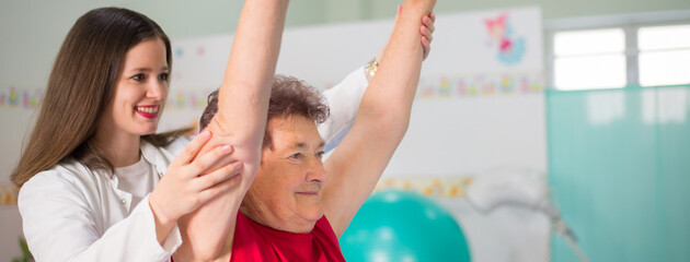 Old senior woman exercising on physical therapy with help of the physiotherapist in the hospital
