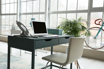 Workplace with modern laptop and landline phone in light office