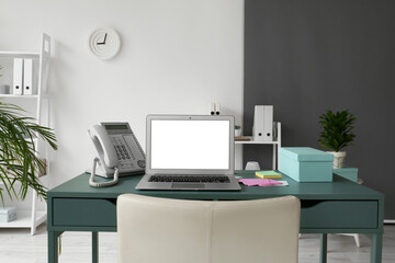 Modern laptop, landline phone and sticky notes on table in office