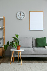 Modern furniture, clock and blank photo frame on wall in room interior