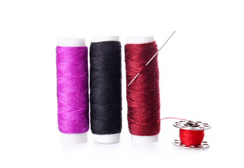 Multicolored thread spools and needle on white background