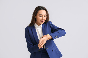 Portrait of young secretary looking at watch on light background